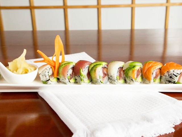 A rainbow roll topped with tuna, salmon and avocado on a long white plate.