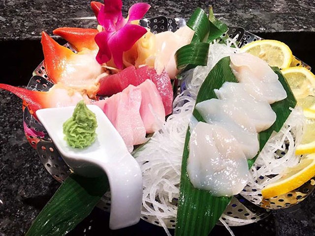 A sashimi platter with tuna, salmon, scallop and orchid garnish.