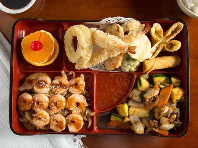 A bento box with tempura, shrimp, gyoza and vegetables.