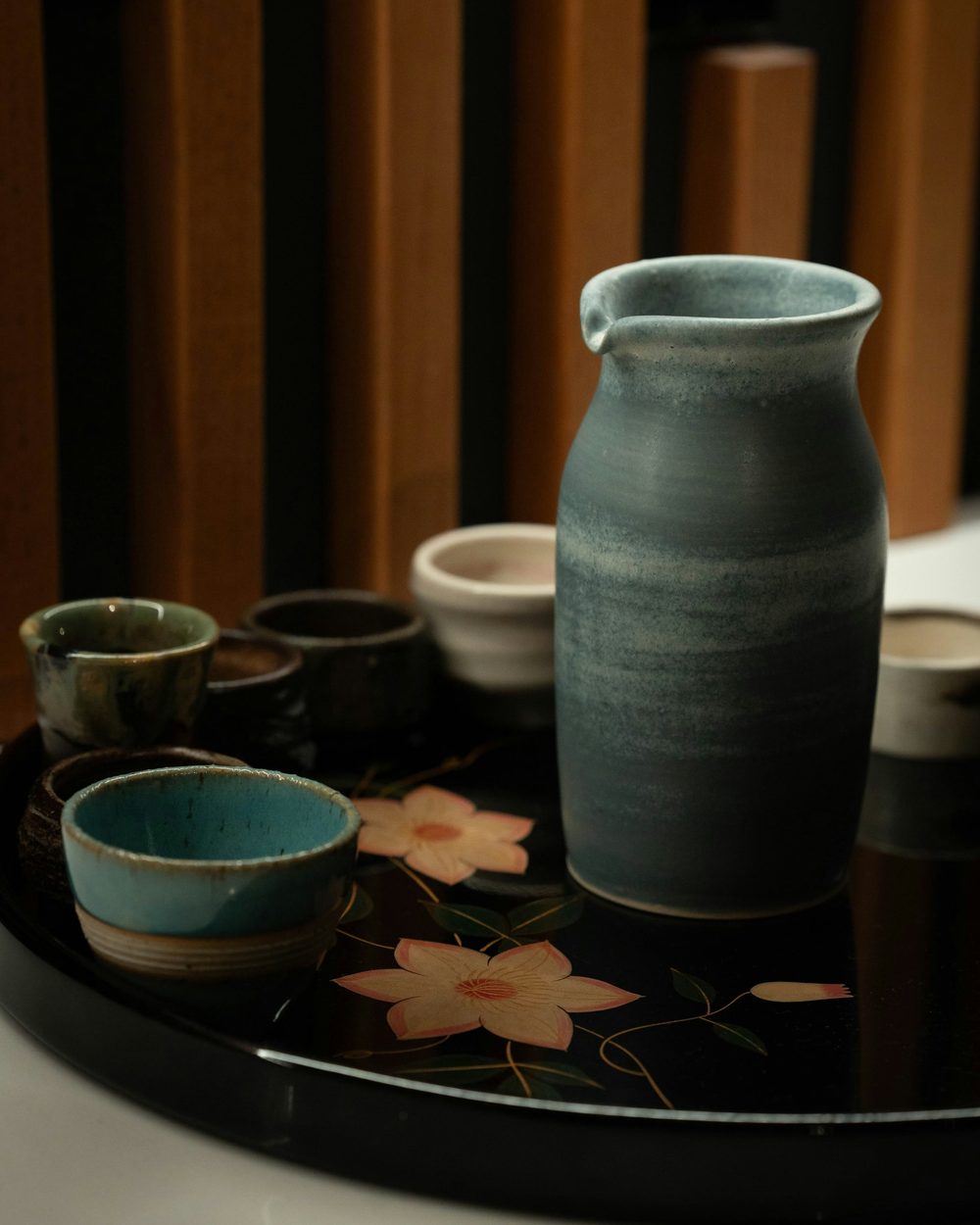 A ceramic sake carafe and cups on a black lacquer tray.