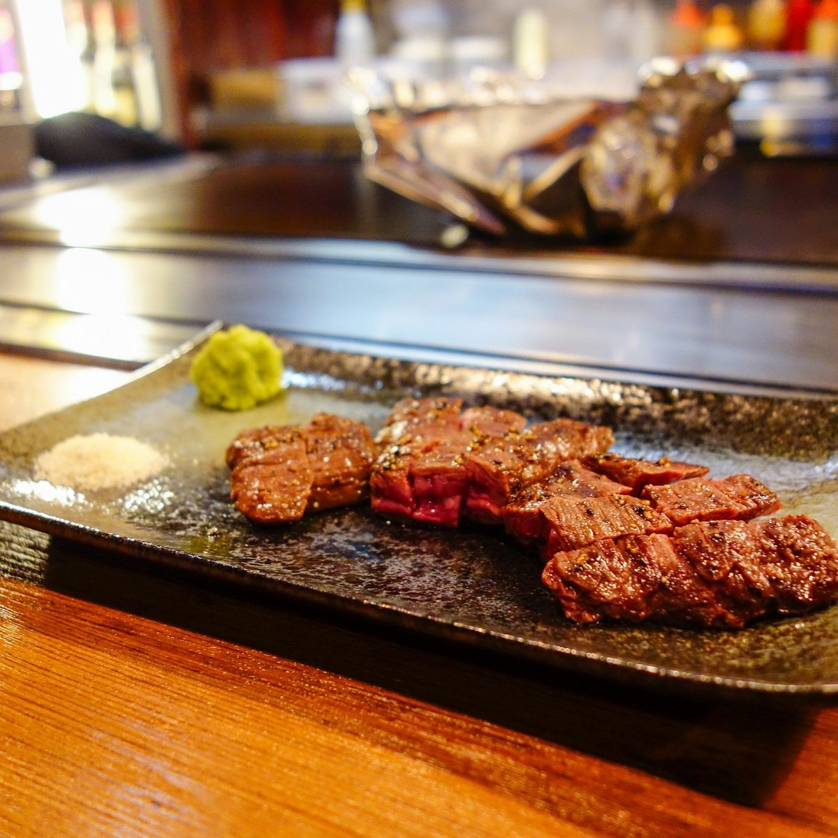 Seared slices of steak on a black plate with wasabi and salt.